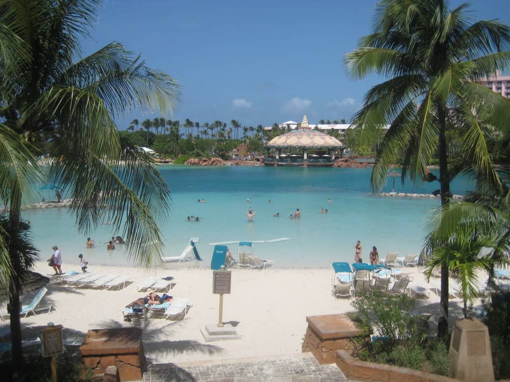 white sand beach and turquoise water fringed by palm trees at a resort. A few people swimming.