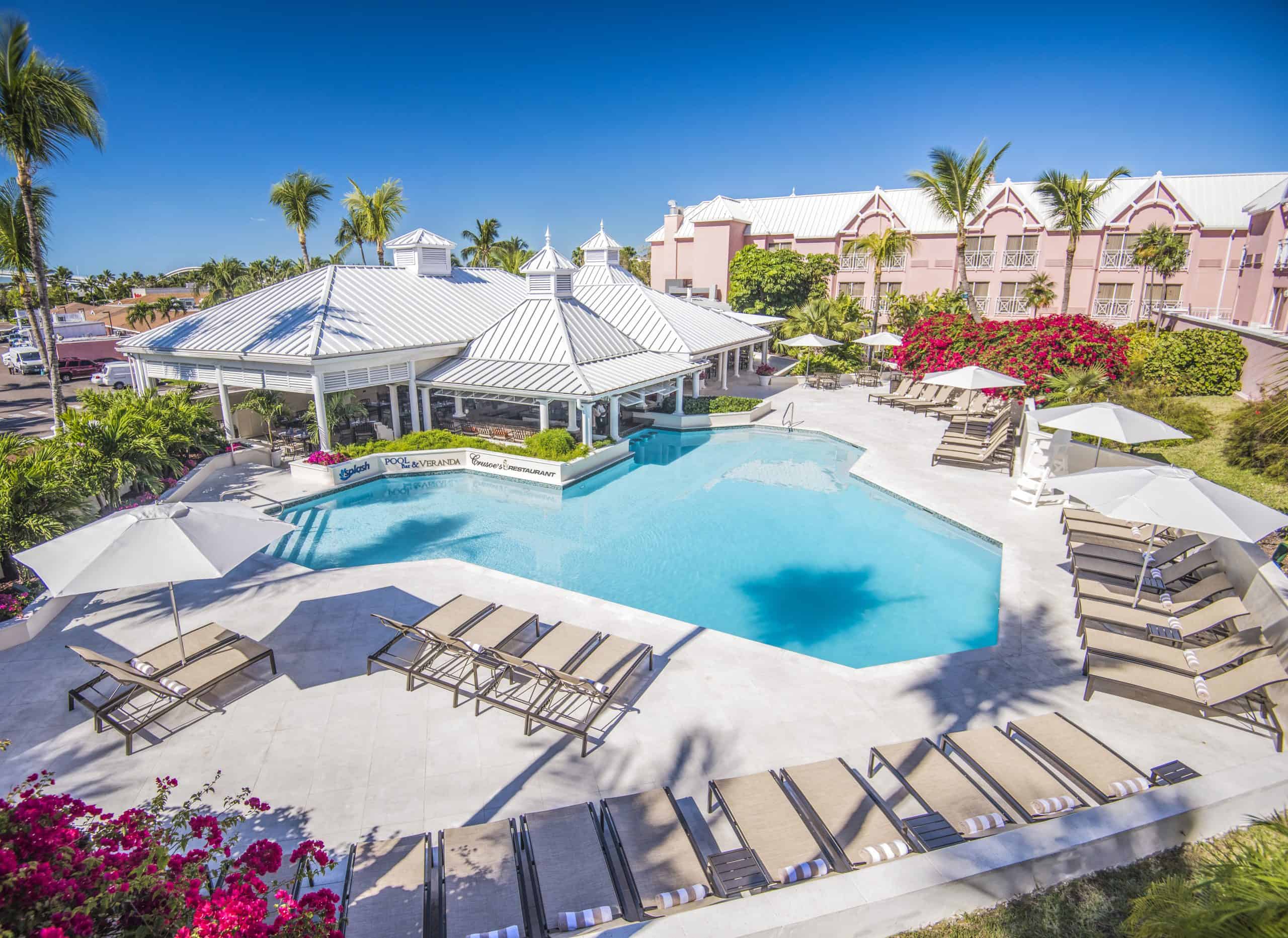 A pink hotel with a swimming pool and palm trees in the foreground