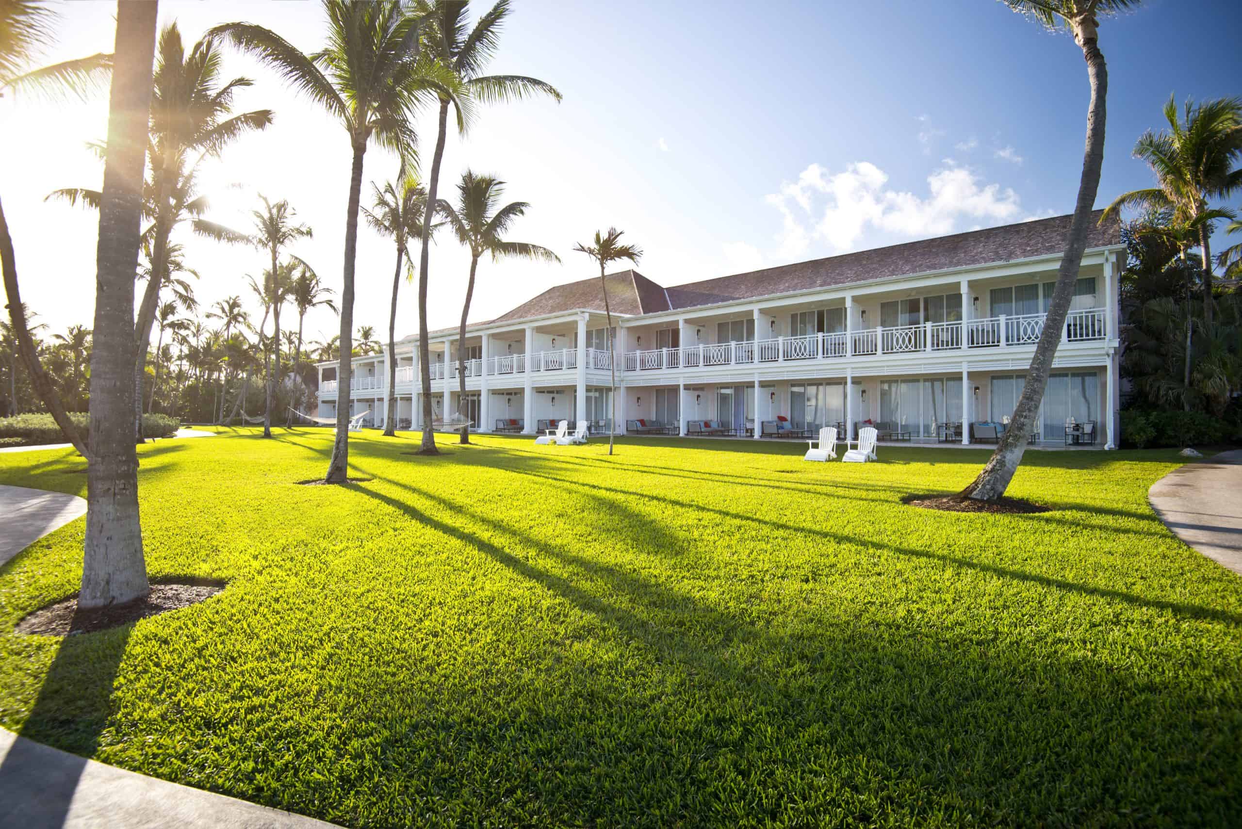 white two storey hotel set on a green lawn with palm trees