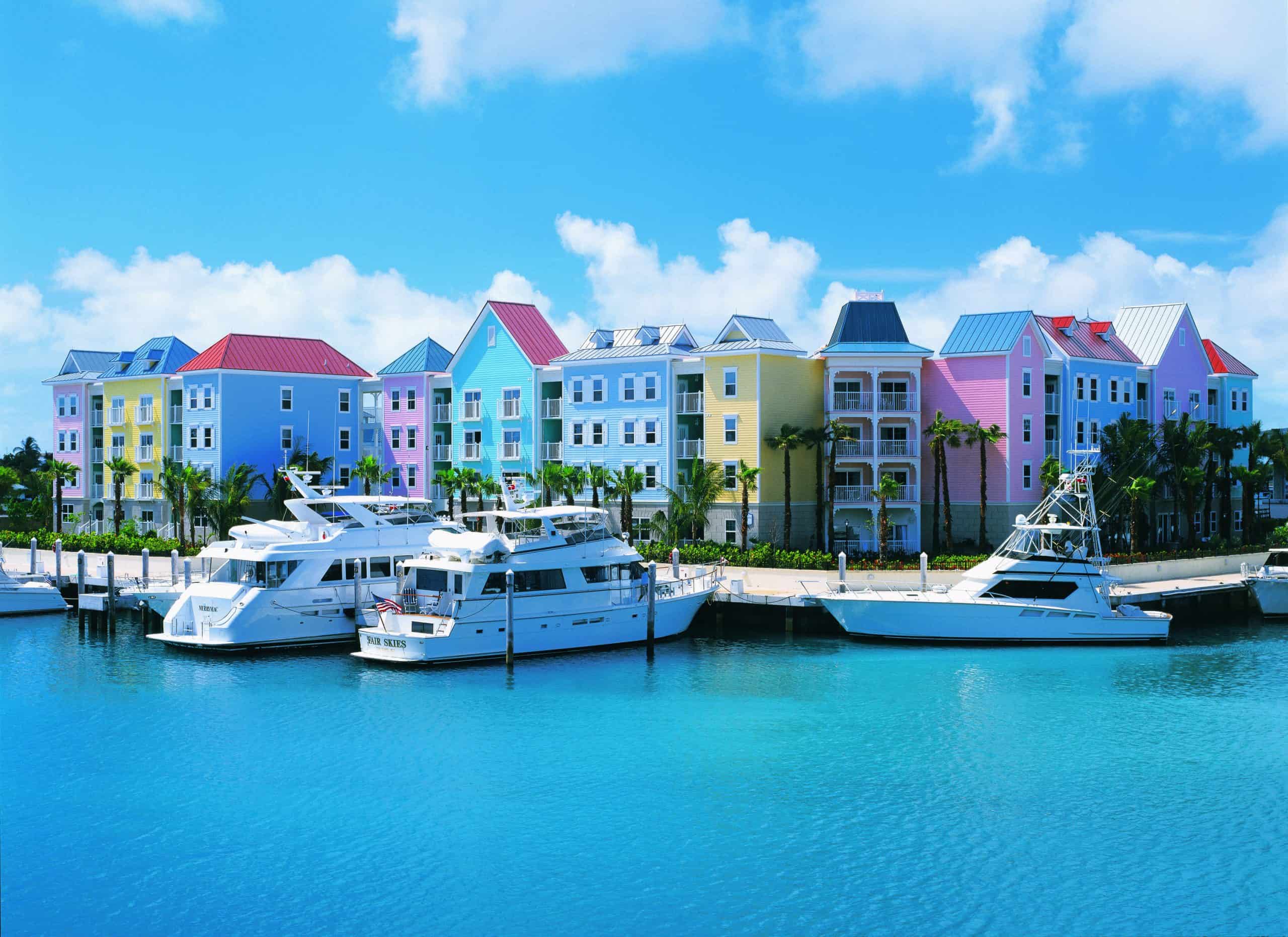 Harbourside pastel-coloured houses with three white yachts moored in front