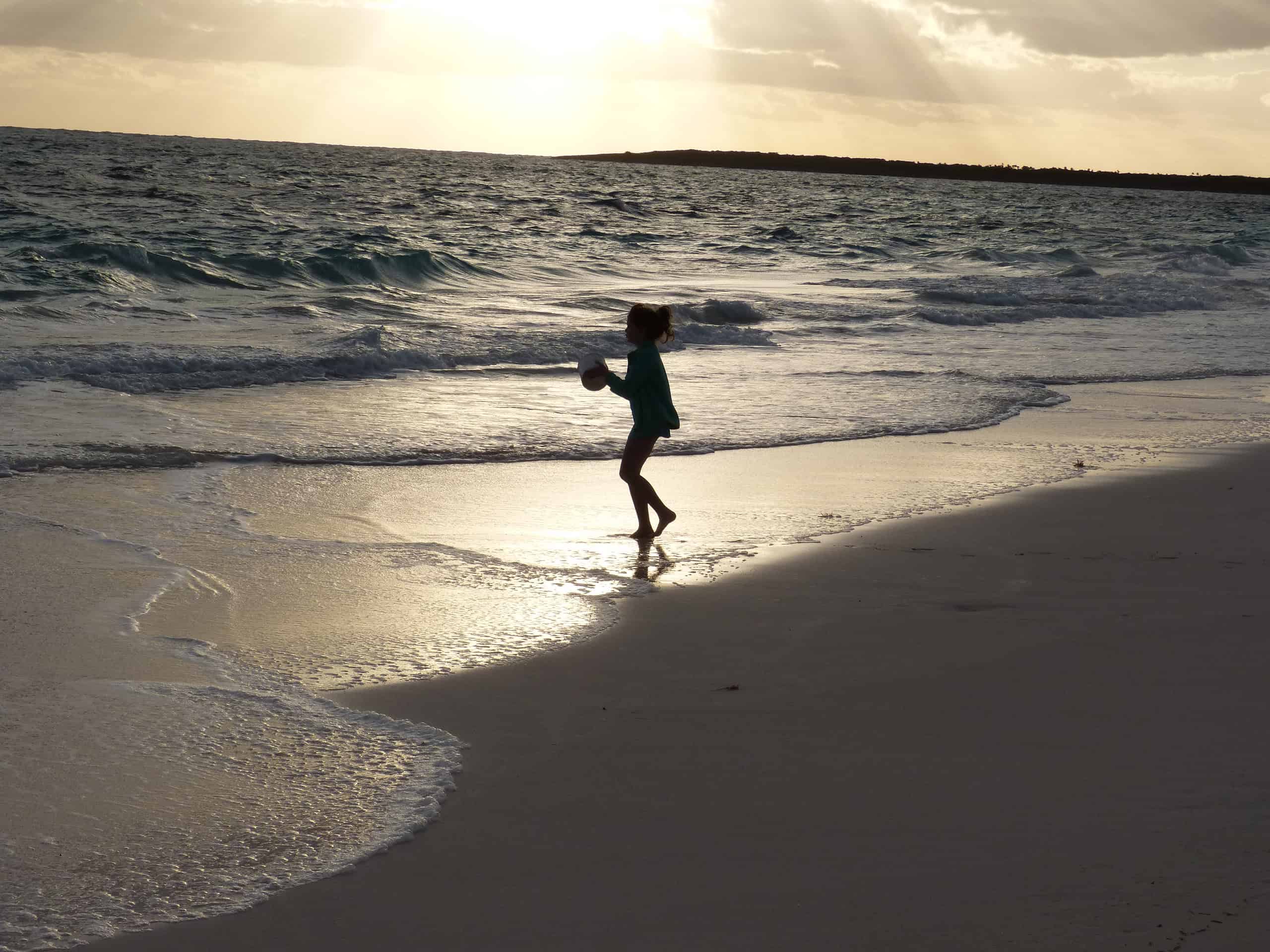 little girl in silhouette playing in the surf on a beach