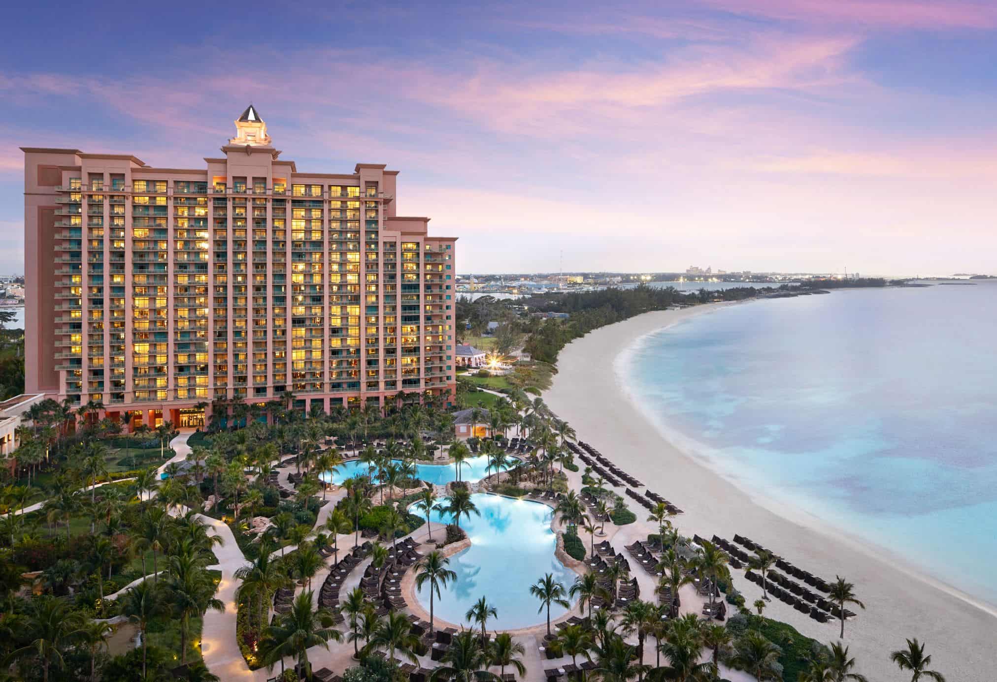 Pink resort hotel by beach at sunset with large swimming pool and palm trees in foreground