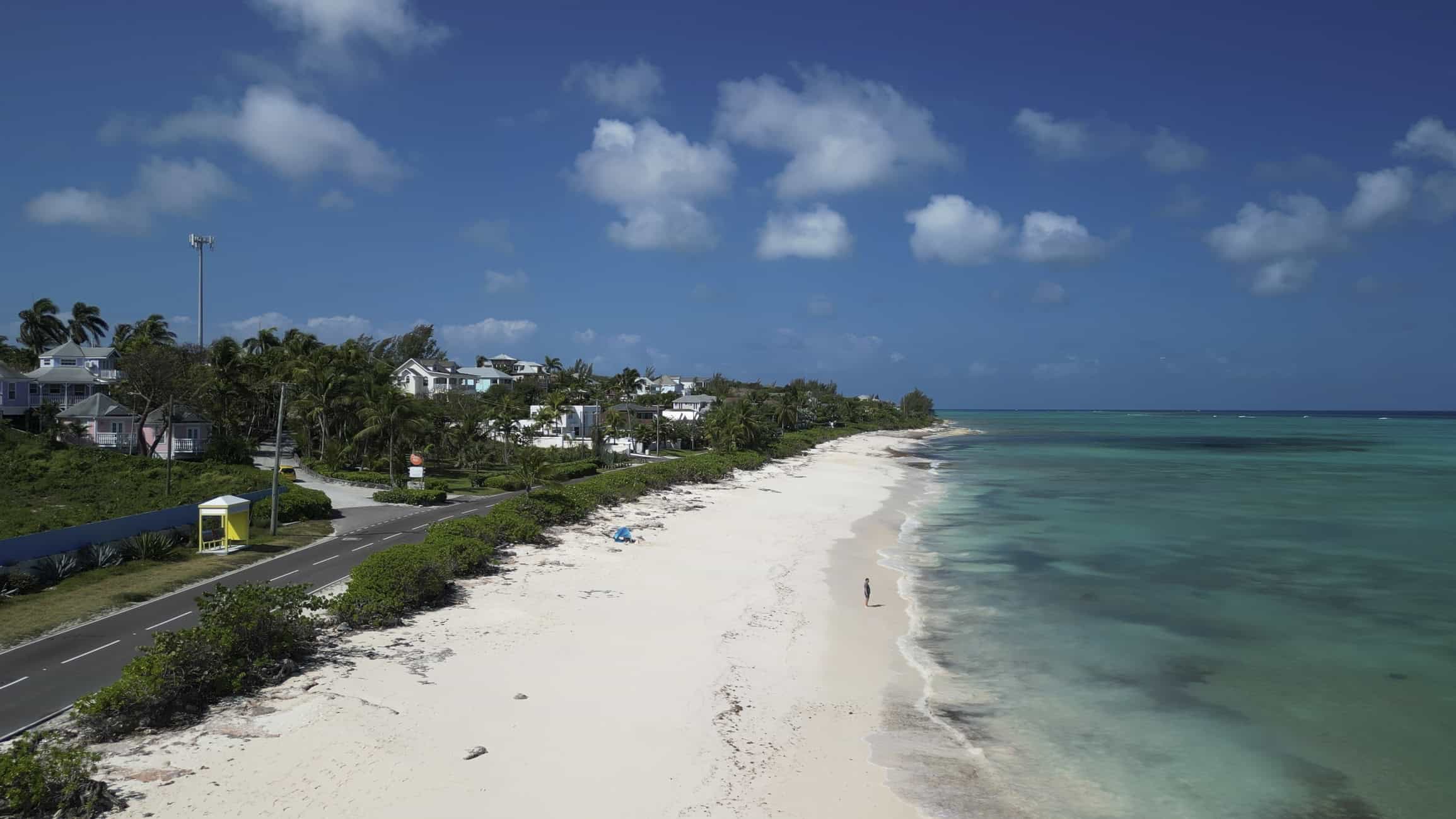 Woman walks down beach near resort and turquoise sea